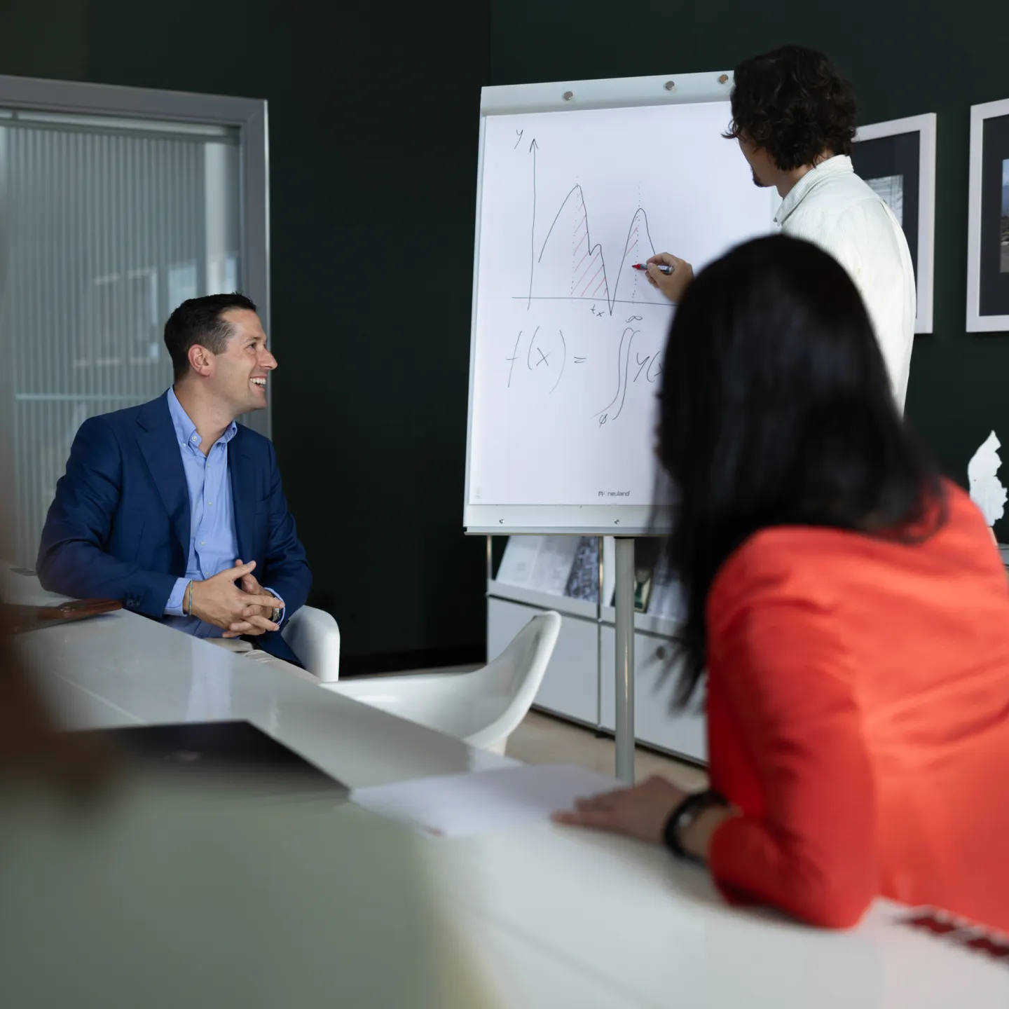 Teilnehmende bei einer Präsentation im Seminarraum, Fokus auf Vortragendem und Flipchart mit Funktionsgleichung.