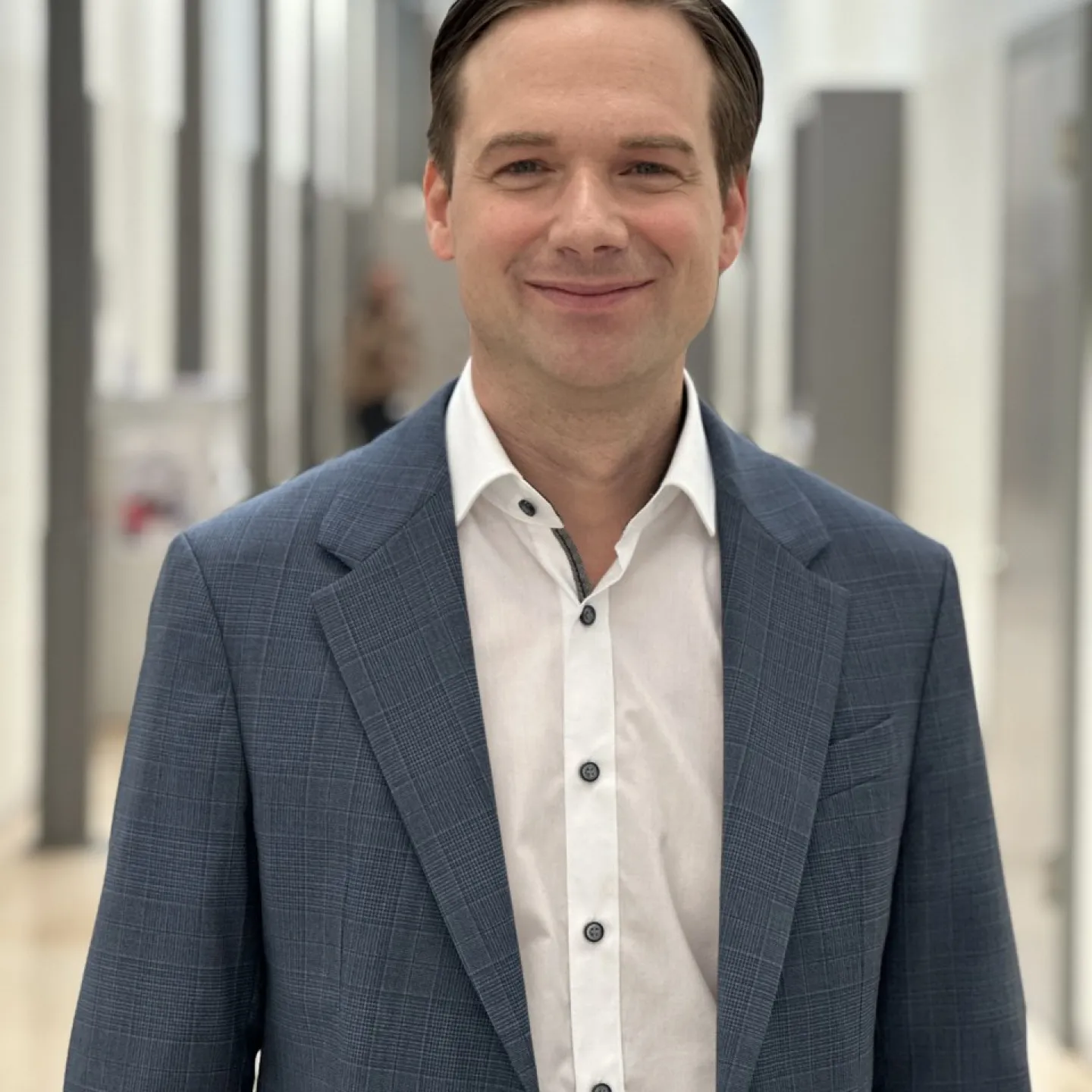 Ein lächelnder Mann in einem blauen Anzug steht in einem modernen, hellen Flur.