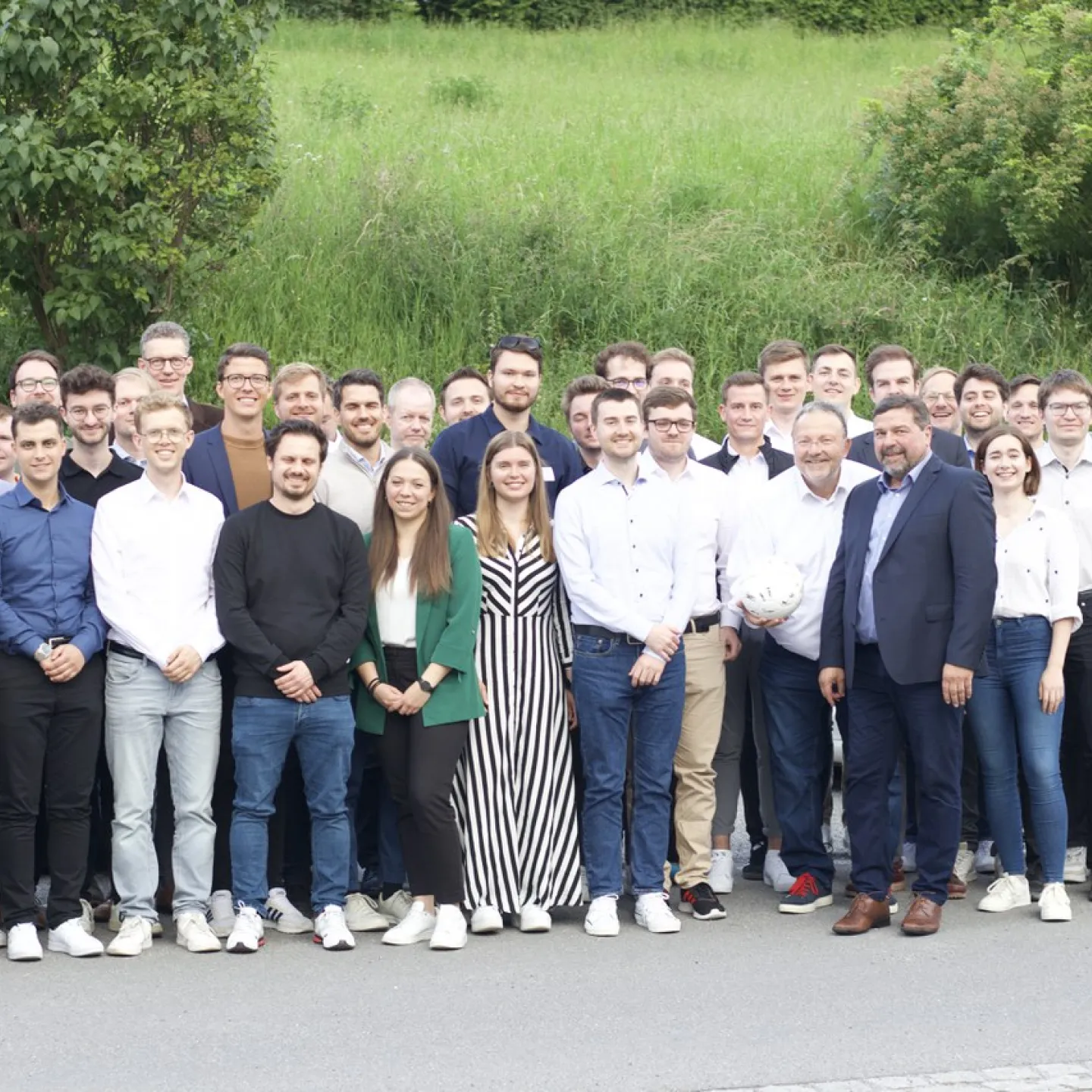 Gruppe von Doktoranden und Professoren steht lächelnd vor einer grünen Wiese bei der Universität Liechtenstein während des Internationalen Doktorandenseminars 2024.