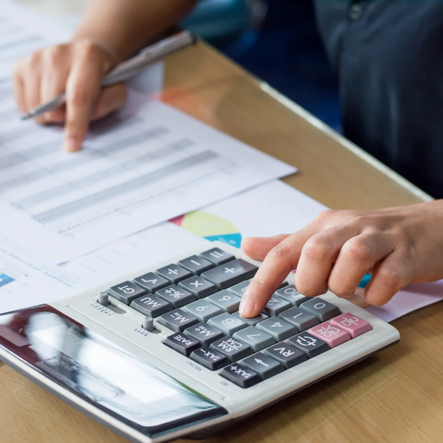 Person sitzt am Tisch mit Taschenrechner und Papier und rechnet