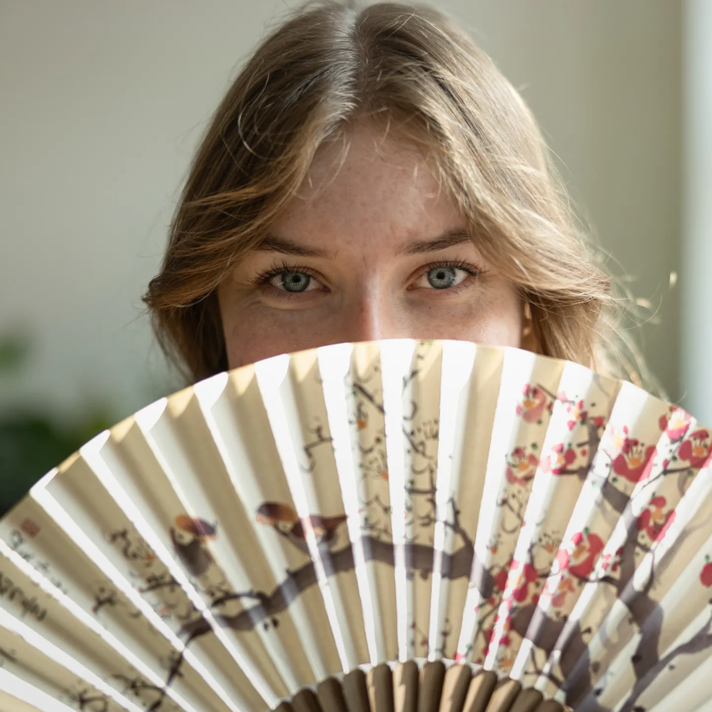 Junge Frau blickt über Fächer mit Blumenmuster in die Kamera.