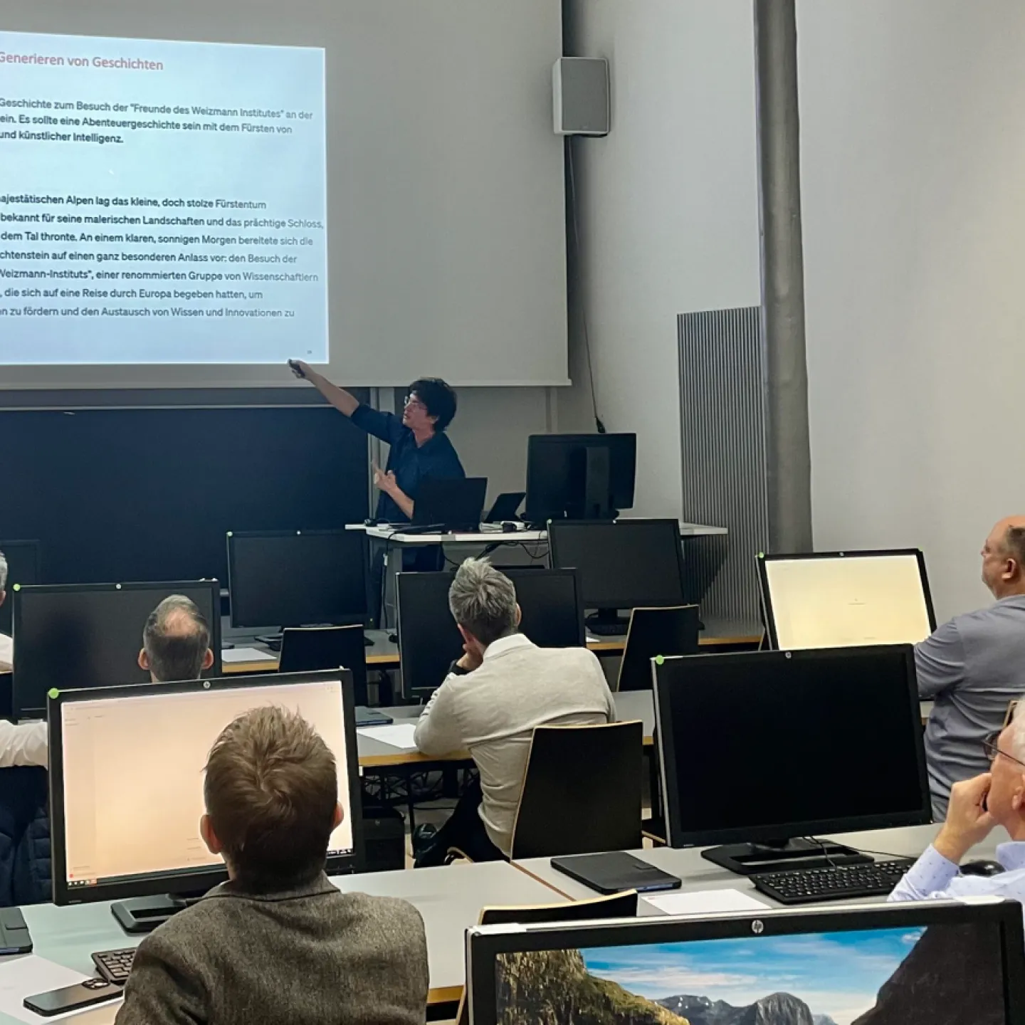 Ein Dozent hält einen interaktiven Workshop an der Universität Liechtenstein. Er zeigt auf eine Präsentation über künstliche Intelligenz, während die Teilnehmenden an Computern sitzen und aufmerksam zuhören.