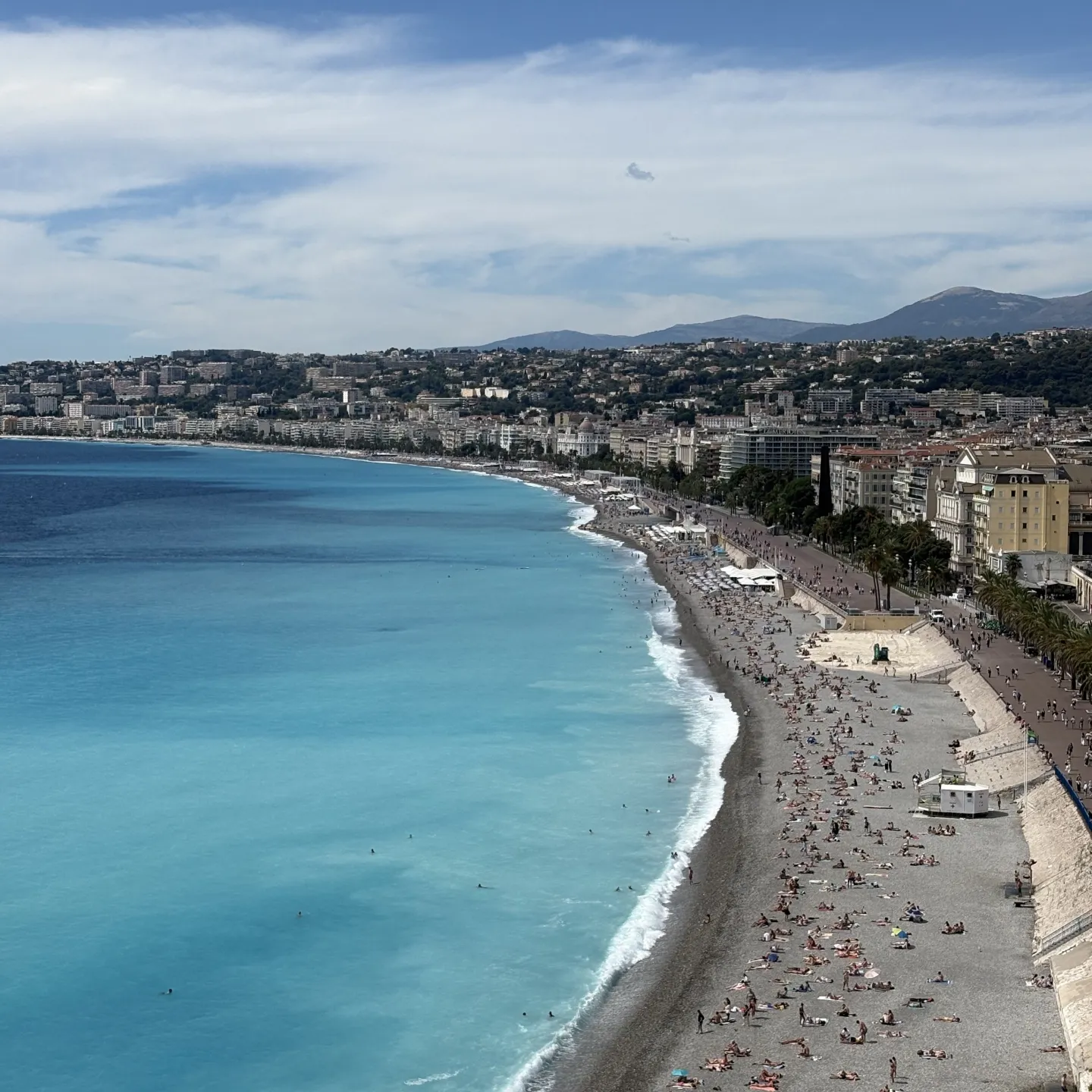 Grau wirkender Strand mit Blauem Wasser und vielen Menschen