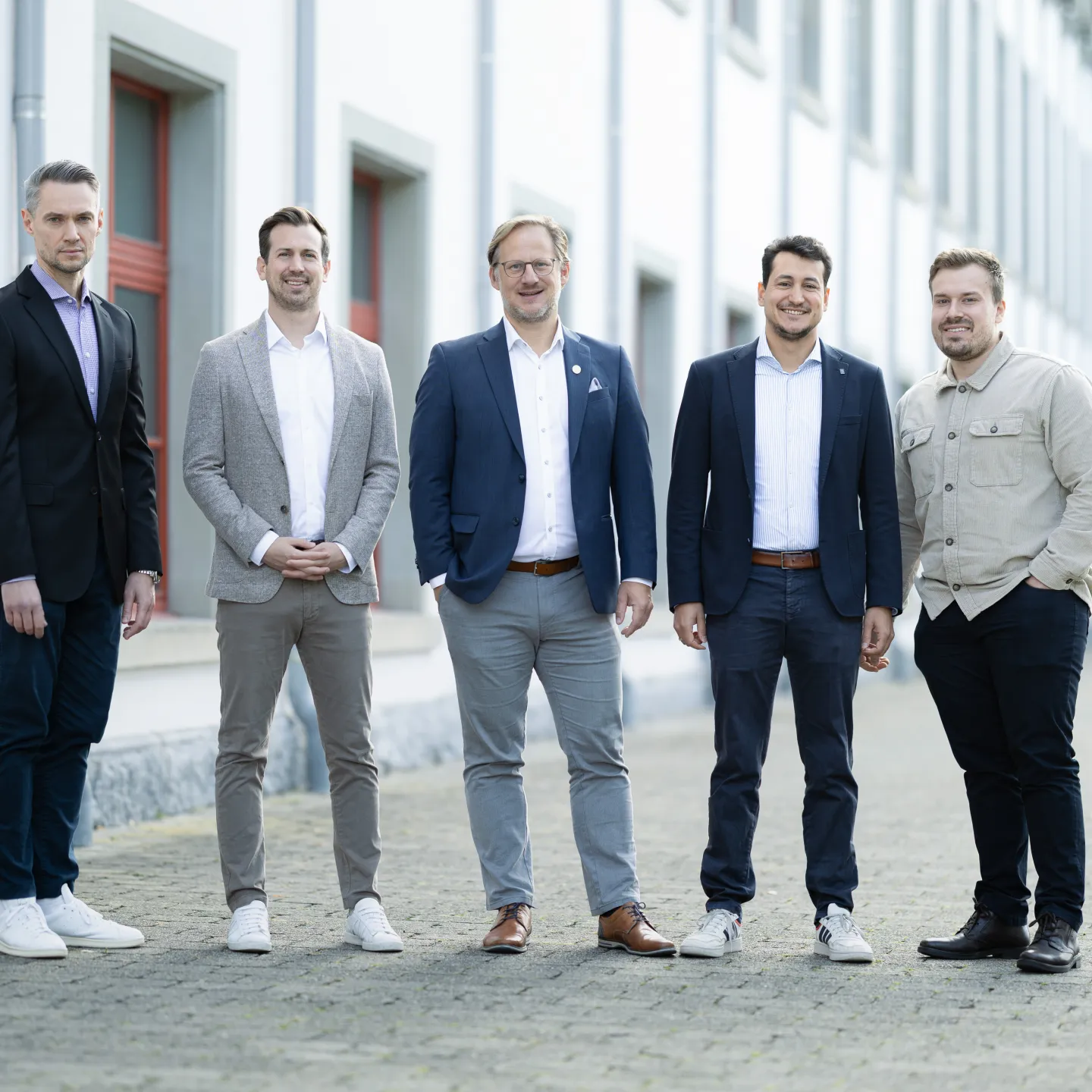 Fünf Mitglieder der Professur für Finanzökonomie stehen vor einem Gebäude der Universität Liechtenstein, business-casual gekleidet, lächelnd und nach vorne gerichtet, Symbol für Teamarbeit in Forschung und Lehre.