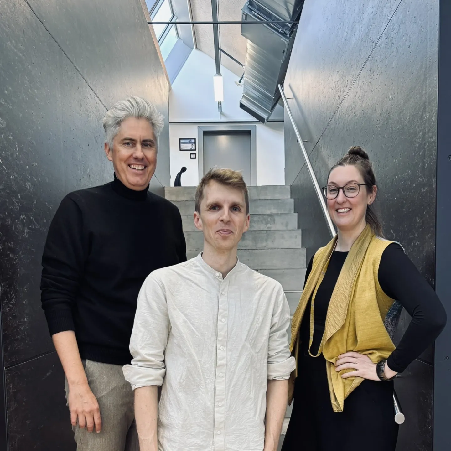 Drei Personen auf einer grau/schwarzen Treppe