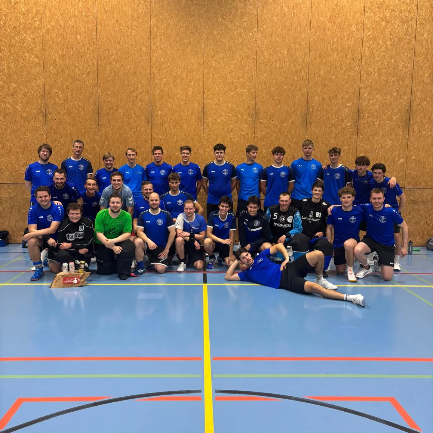 Gruppenfoto einer Handballmannschaft in blauen Trikots in einer Sporthalle.