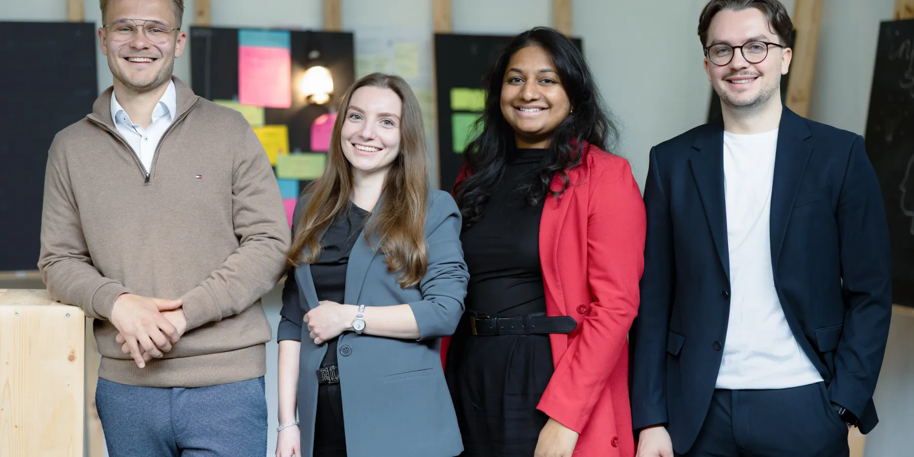 Vier Studierende des Master Entrepreneurship, Innovation und Leadership der Universität Liechtenstein posieren gemeinsam im modernen Campusgebäude – Fokus auf studentische Vielfalt und Gemeinschaft.