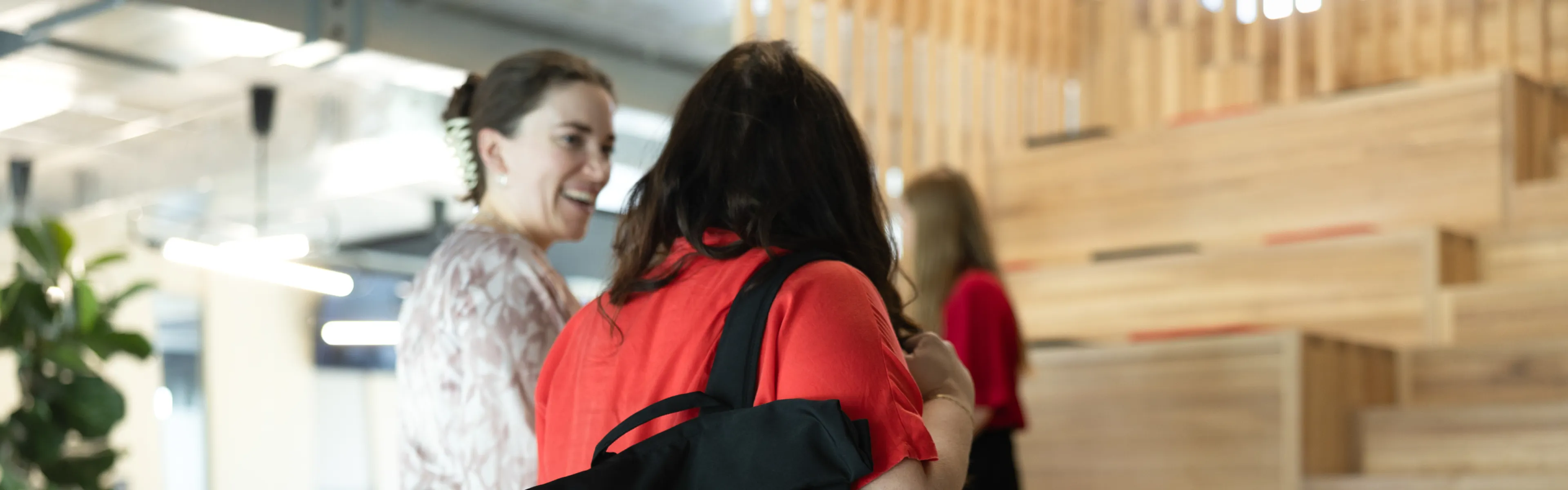 Studierende mit Uni-Rucksack stehen vor den Sitzstufen, im Hintergrund entspannte Gesprächsszene.