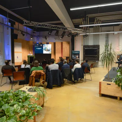 Publikum verfolgt aufmerksam eine Präsentation in einem modern gestalteten Veranstaltungsraum der Universität Liechtenstein.