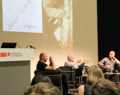 Drei Männer sitzen in Sesseln auf dem Podium und diskutieren