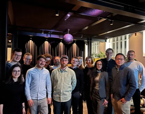 Eine Gruppe von Alumni der Universität Liechtenstein steht lächelnd in einem modernen Veranstaltungsraum zusammen. Im Hintergrund sind eine Bühne und eine Discokugel zu sehen.