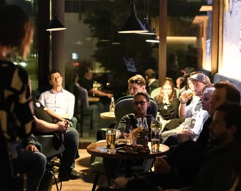 Alumni-Treffen in gemütlicher Atmosphäre: Eine Gruppe von Menschen sitzt in einer Lounge, unterhält sich und genießt Getränke.