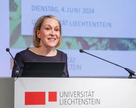 Eine Frau hält eine Rede am Rednerpult der Universität Liechtenstein. Im Hintergrund ist eine Präsentationsfolie mit dem Datum 4. Juni 2024 zu sehen.