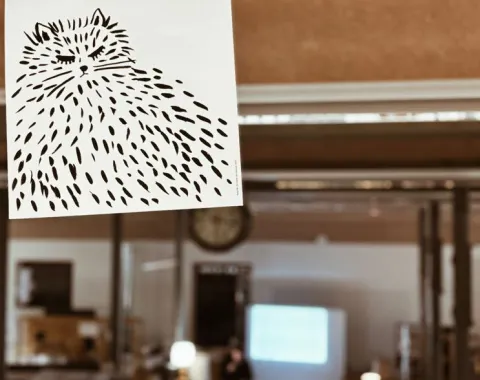 Ein handgezeichnetes Bild einer flauschigen Katze mit dem Text "I don't want to talk about it" hängt vor einem unscharfen Hintergrund, der einen Raum mit einer Präsentation zeigt.