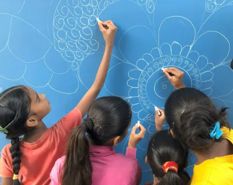 Kinder zeichnen mit Kreide auf eine blaue Tafel kunstvolle Muster.