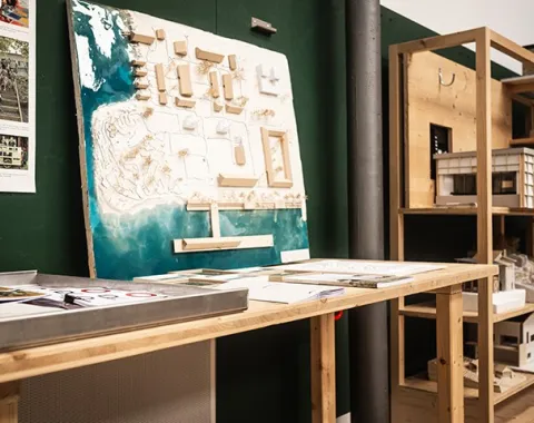 Ein Architekturmodell auf einem Holztisch in einem Studio der Universität Liechtenstein. Im Hintergrund sind weitere Modelle und Materialien zu sehen.
