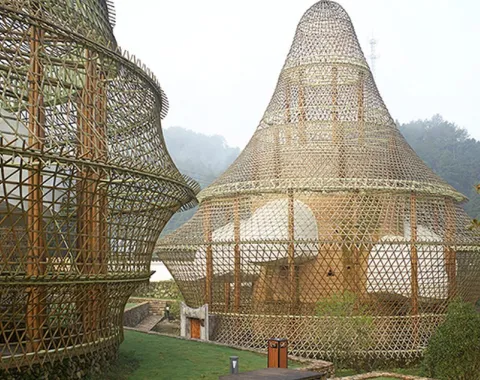 Bambusarchitektur mit kuppelförmigen Strukturen in einer grünen Landschaft. Die Konstruktionen zeigen innovative Nutzung natürlicher Materialien und verbinden traditionelle Bauweisen mit modernem Design.