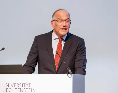 Ein Redner im Anzug steht am Podium der Universität Liechtenstein und hält eine Präsentation.