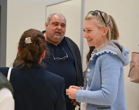 Eine Gruppe von Personen unterhält sich in einem hellen Raum während der Erasmus-Days an der Universität Liechtenstein. Eine Frau im Vordergrund trägt eine blaue Jacke und lächelt.