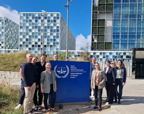 Gruppe von Studierenden des Executive Master of Laws (LL.M.) im Wirtschaftsstrafrecht vor dem Internationalen Strafgerichtshof in Den Haag, lächelnd und posierend vor dem Gebäude mit dem Logo des Gerichtshofs.