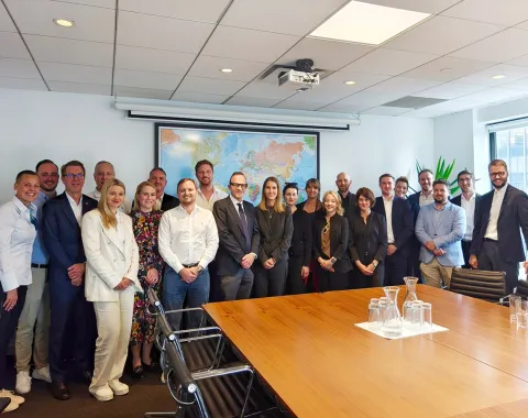 Gruppenfoto von Studierenden und Dozenten des Executive Master of Laws (LL.M.) während einer Studienreise in einem Konferenzraum mit Weltkarte im Hintergrund.