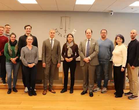 Eine Gruppe von Studierenden und Dozenten des Executive Master of Laws (LL.M.) im Wirtschaftsstrafrecht steht in einem Konferenzraum vor einer Wand mit dem Logo des EFTA Court. Sie sind formell gekleidet und lächeln in die Kamera.
