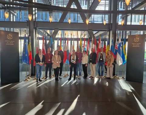 Gruppe von Studierenden des Executive Master of Laws (LL.M.) im Wirtschaftsstrafrecht steht vor einer Reihe internationaler Flaggen im Gebäude des Internationalen Strafgerichtshofs in Den Haag.