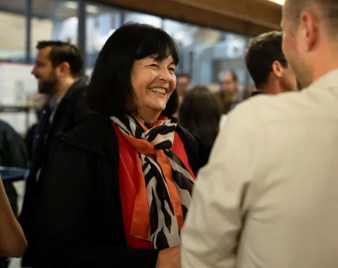 Eine Person lächelt und unterhält sich mit einer anderen Person in einem belebten Raum während des LSA Sommerfests an der Universität Liechtenstein. Im Hintergrund sind weitere Gäste zu sehen.