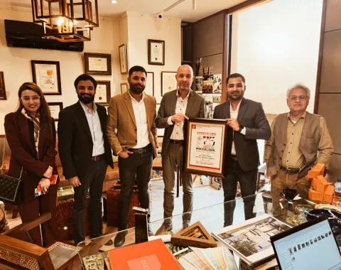 Eine Gruppe von sechs Personen steht in einem Büro, eine Person hält eine gerahmte Auszeichnung. Im Hintergrund sind Zertifikate und Auszeichnungen an der Wand zu sehen.