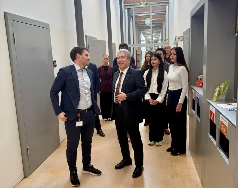 Gruppe von Menschen in einem modernen Universitätsflur, darunter ein Mann im Anzug, der spricht. Im Hintergrund sind weitere Personen, die aufmerksam zuhören. Die Szene zeigt einen offiziellen Besuch und Austausch an der Universität Liechtenstein.