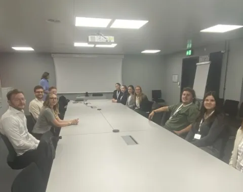 Studierende der Universität Liechtenstein sitzen in einem Konferenzraum bei Ivoclar in Schaan. Im Hintergrund ist eine Präsentationsleinwand zu sehen.
