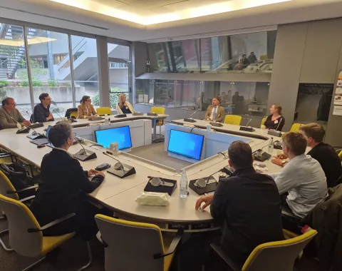 Studierende des Executive Master of Laws (LL.M.) im Wirtschaftsstrafrecht sitzen in einem modernen Konferenzraum des Europarats in Straßburg. Sie nehmen an einer Diskussion teil, geleitet von einem Vortragenden. Laptops und Notizen sind auf dem Tisch verteilt.