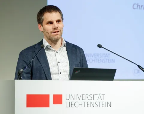 Der Rektor der Universität Liechtenstein Christian Frommelt steht an einem Redepult mit dem Logo der Universität aufgedruckt.