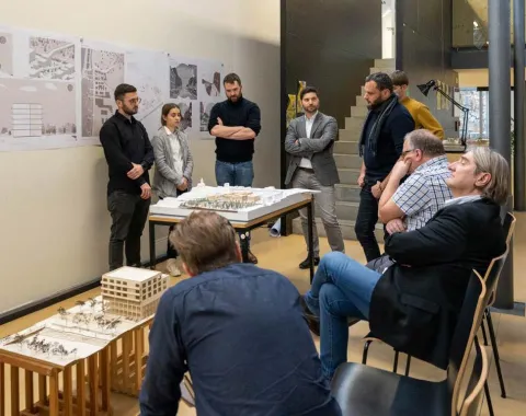 Mehrere Menschen bei einer Präsentation von Studierenden mit einem Architekturmodell