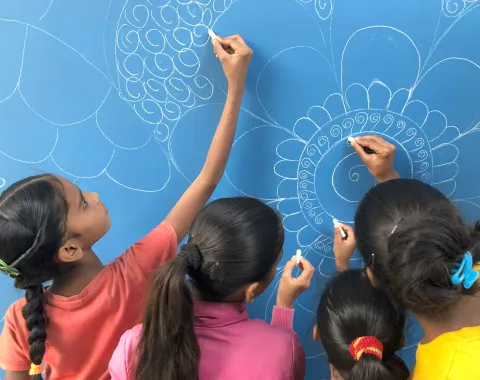 Mehrere Kinder zeichnen mit Kreide ein großes, ornamentales Muster auf eine blaue Tafel.