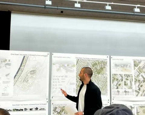 Student in Präsentationssituation mit Plänen im Hintergrund