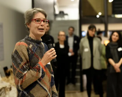 Eine Frau mit roter Brille und buntem Pullover spricht in ein Mikrofon