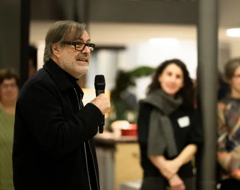 Ein Mann spricht vor einer Gruppe von Menschen mit einem Mikrofon in der Hand 