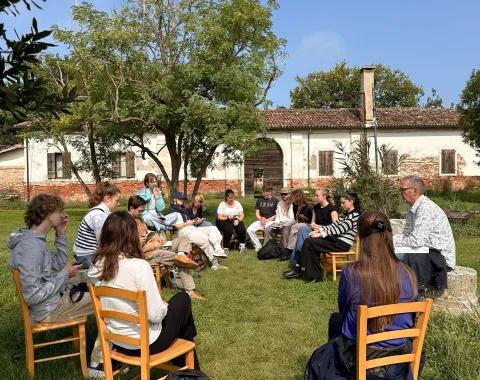 Gruppe junger Menschen sitzen im Freien in einem Stuhlkreis und diskutieren