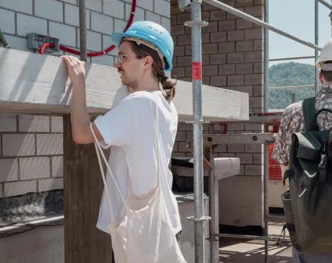 Ein Mann mit einem Bauhelm und einer Baumwolltasche inspiziert eine Baustelle 