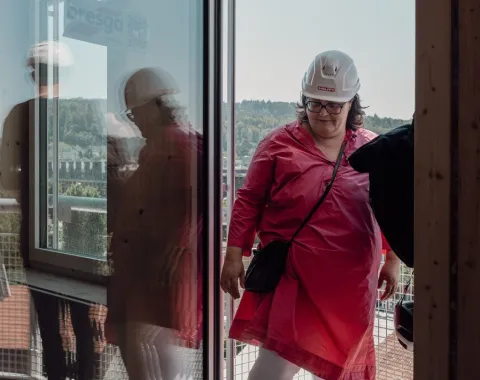 Eine Frau mit pinkem Kleid und einem weissen Bauhelm bei einer Baustellenbegehung 