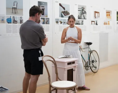 Ein Mann und eine Frau stehen in einer Ausstellung mit einem Kaffeehausstuhl im Vordergrund 