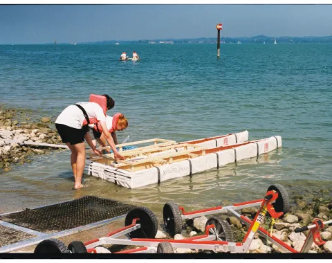Zwei Personen lassen ein selbstgebautes Boot zu Wasser. 