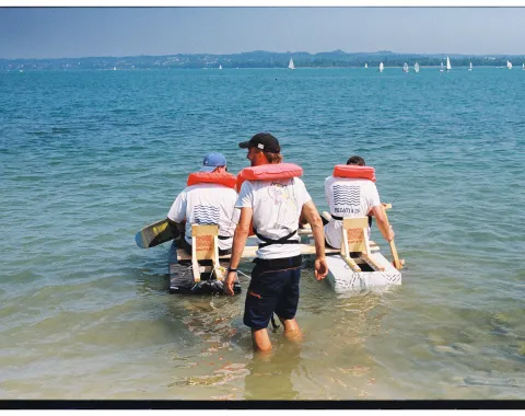 Zwei Menschen mit Schwimmweste in einem selbstgebauten Boot. 