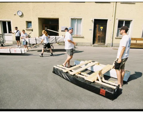 Mehrere Menschen transportieren selbstgebaute Boote aus Holz und Plastikfolie. 