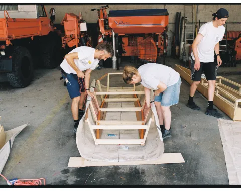 Drei Personen in einer Werkstatt, die an einem Boot arbeiten. 