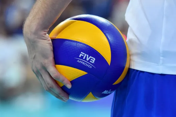 Eine Person hält einen FIVB-geprüften Volleyball fest, bereit für den nächsten Aufschlag auf einem Indoor-Volleyballfeld.