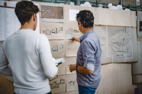 Dozent und Student besprechen architektonische Pläne an einer Präsentationswand – individuelle Betreuung im Designstudium an der Universität Liechtenstein.