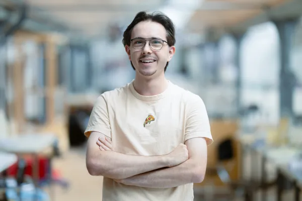 Student der Universität Liechtenstein mit gelbem Pullover lächelt in die Kamera – Campusaufnahme in freundlicher Lernumgebung