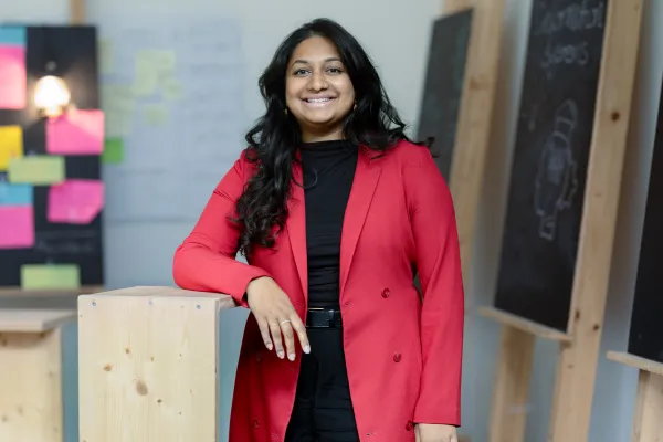 Studentin des Master Entrepreneurship, Innovation und Leadership der Universität Liechtenstein im roten Blazer lächelt in die Kamera – Campusaufnahme in freundlicher Lernumgebung.